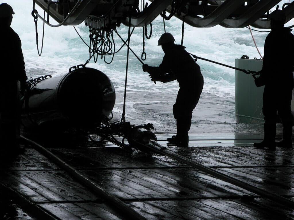 Image: Silhouettes of persons recovering source (gun) array on seismic survey vessel. Sources (gun) are used to produce underwater acoustic sound waves with high pressure air.Location: Norway. 