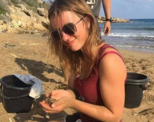 Dr Eleanor Mullen holds a turtle hatchling on a beach in Cyprus.